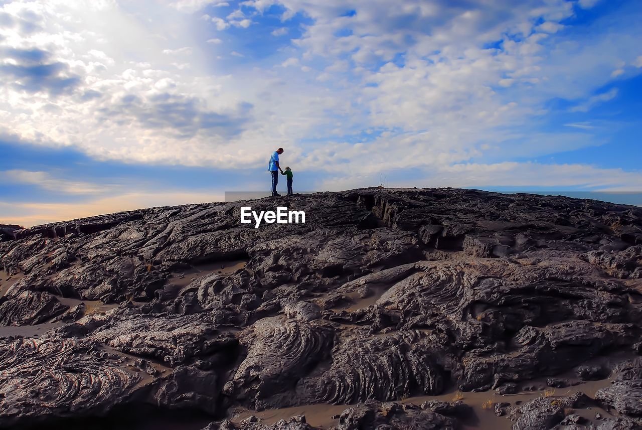Father and daughter standing on rock formation against sky