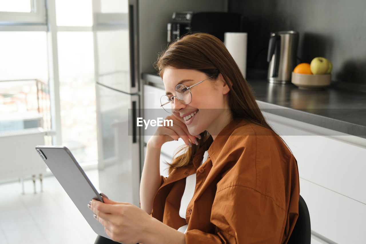 young woman using mobile phone while sitting on table at home