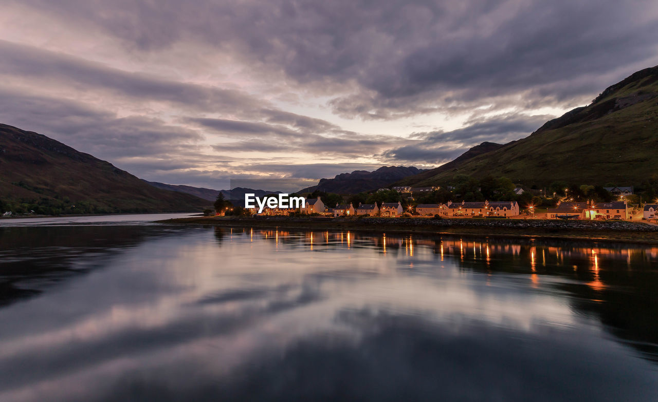 Scenic view of lake by illuminated houses against sky at dusk