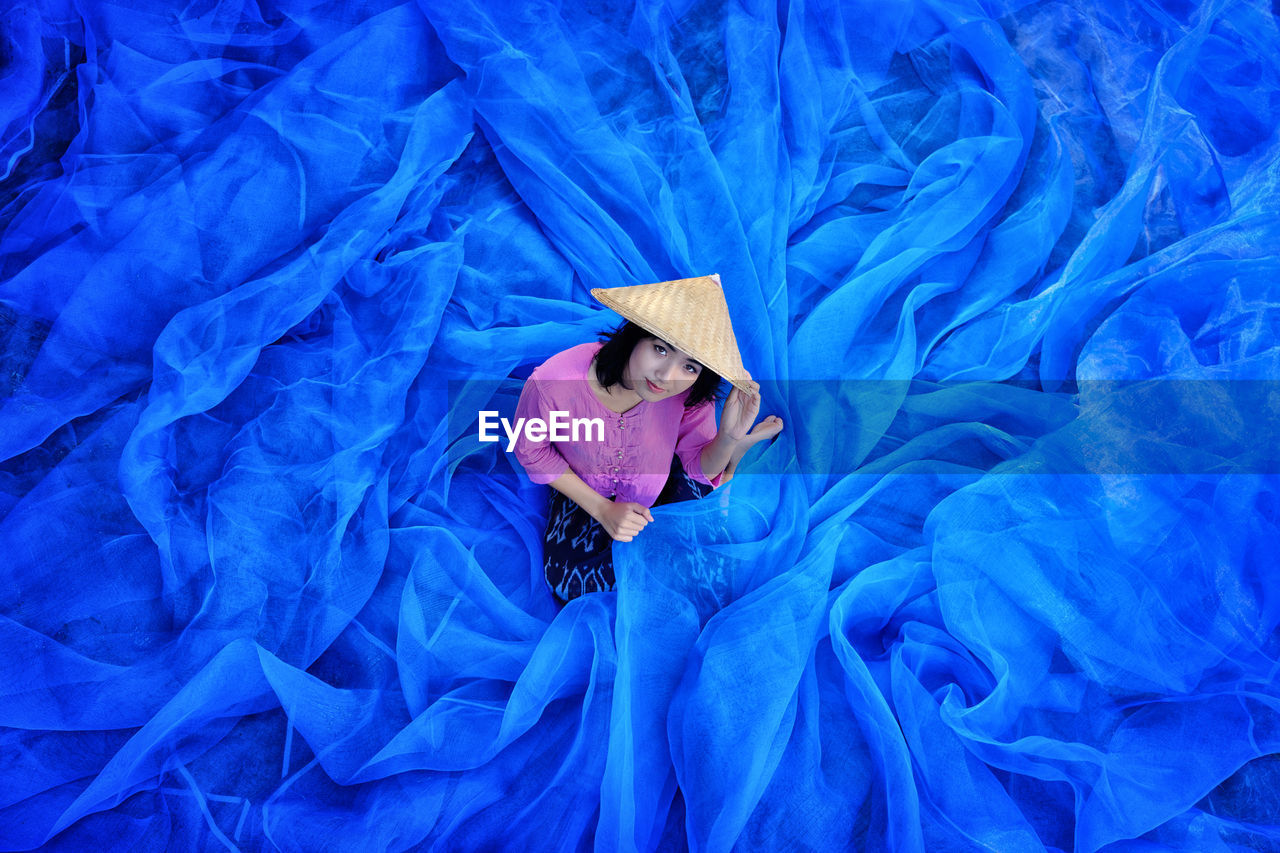 Young woman wearing asian style conical hat holding blue tulle netting