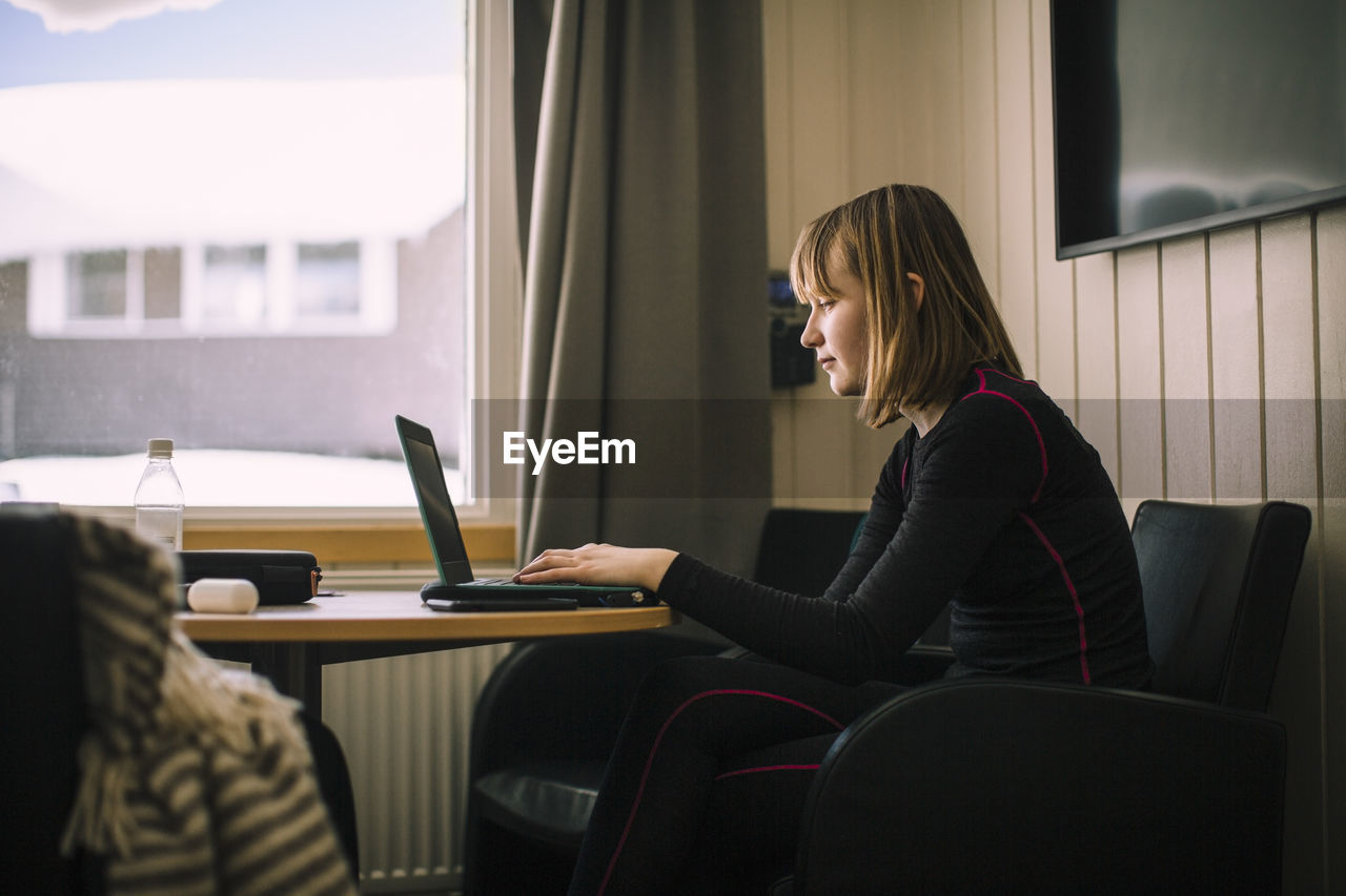 Teenage girl using laptop while doing homework in living room