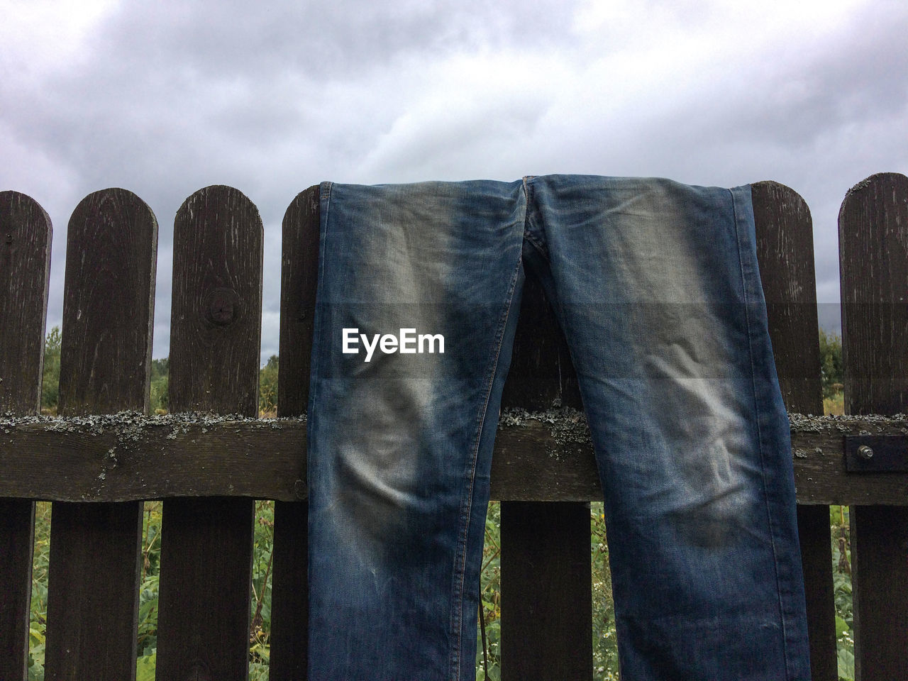 Jeans on wooden fence against cloudy sky