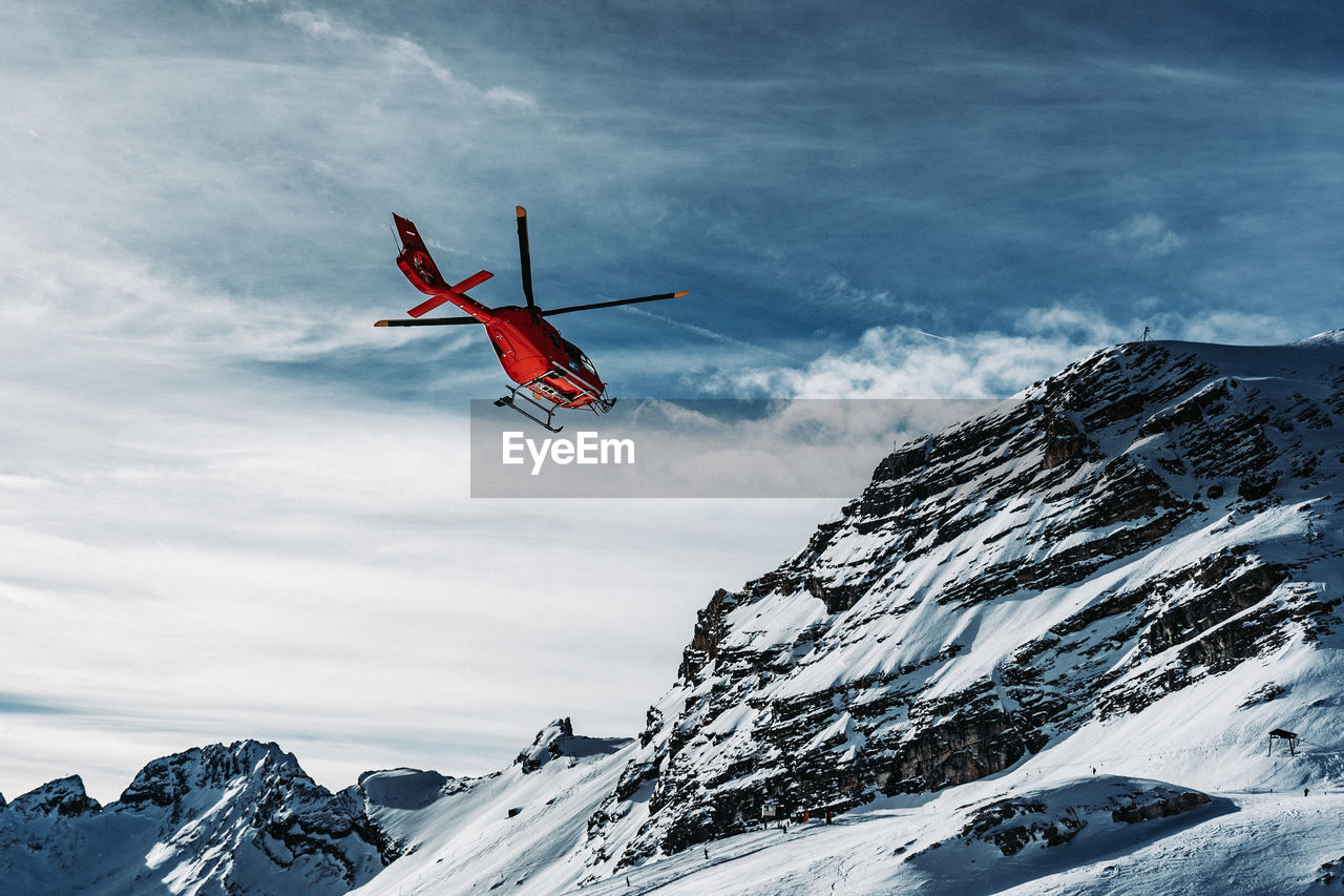 Helicopter flying over snowcapped mountains against sky