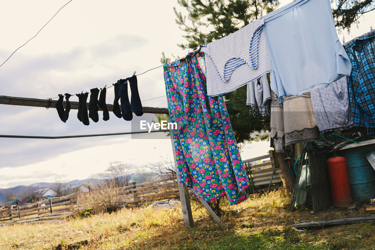 clothesline, drying, laundry, hanging, clothing, clothespin, textile, nature, sky, day, plant, no people, housework, multi colored, outdoors, chores, sunlight, grass, architecture, tree, rope, building exterior, built structure, washing, low angle view, landscape, cleaning