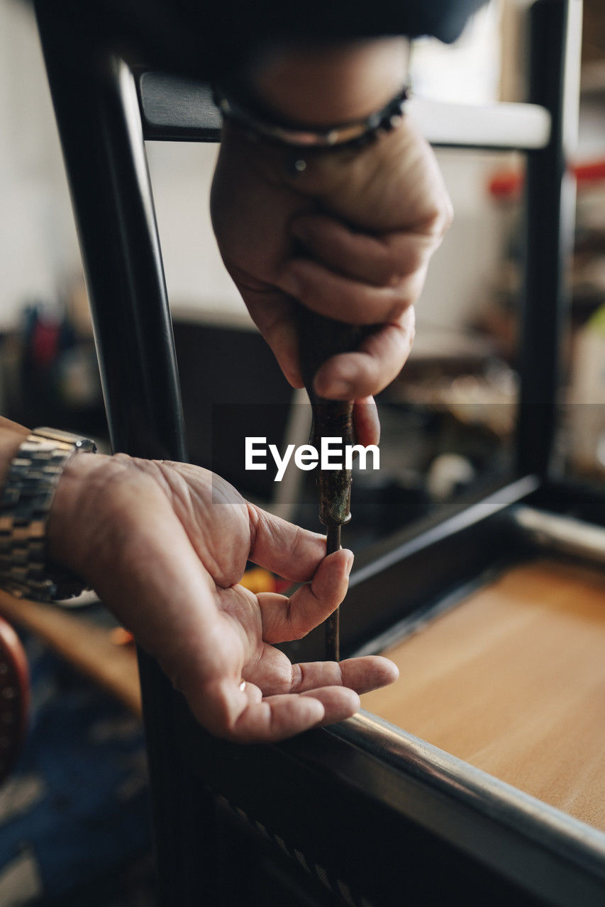 Hands of senior male owner repairing chair with tool while working at antique store