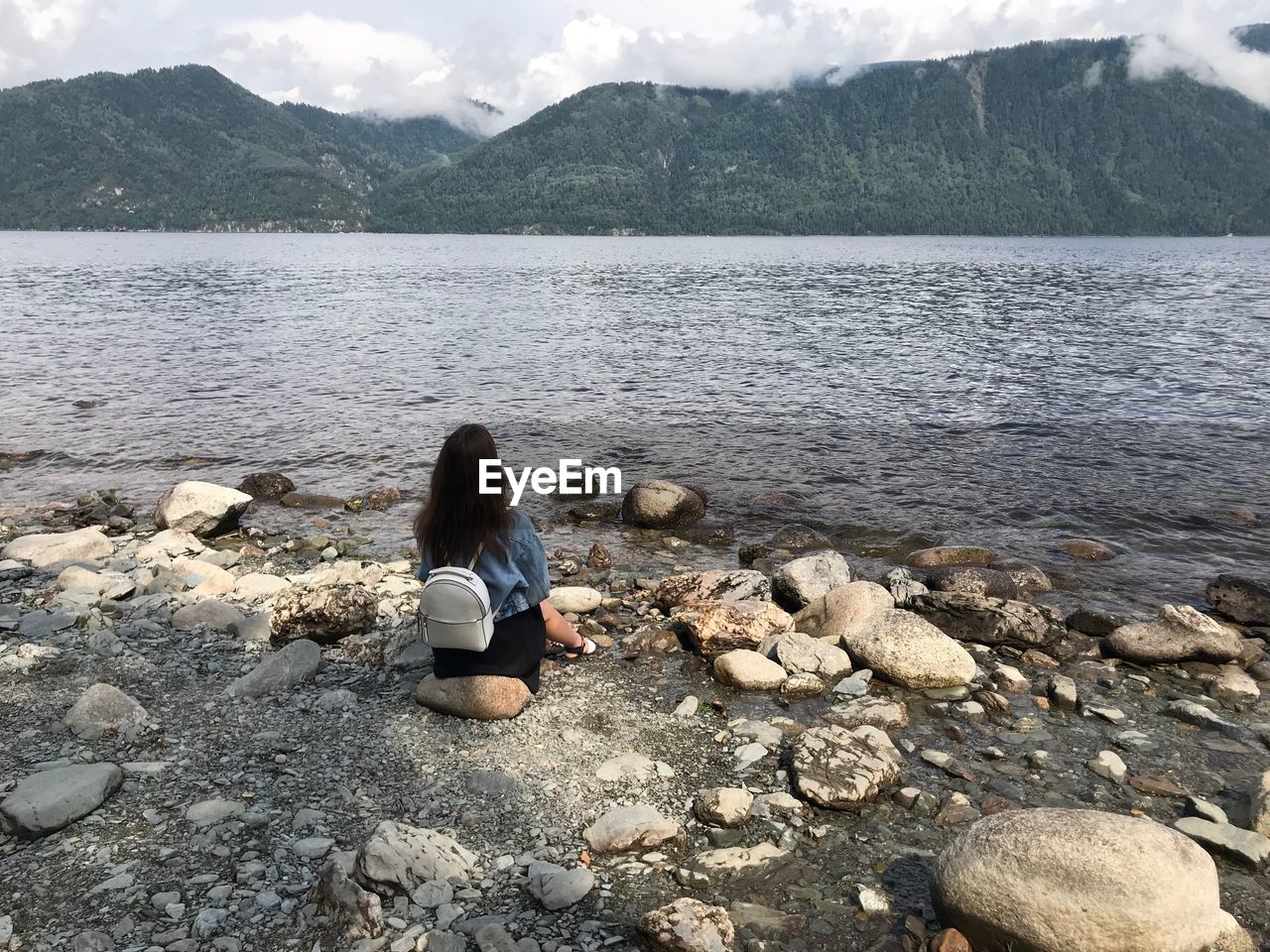 Rear view of woman sitting on rock at river