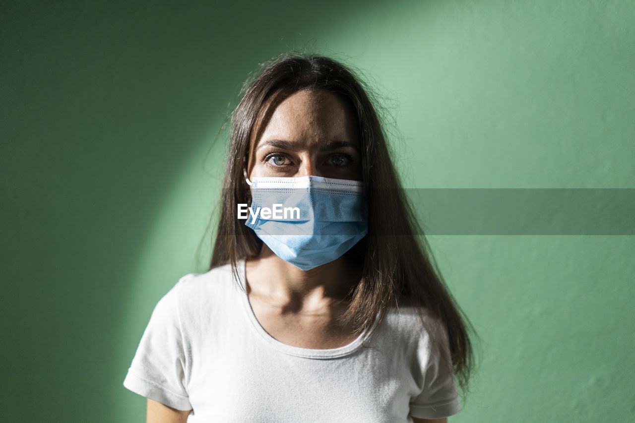 Young woman wearing protective face mask against green wall during covid-19