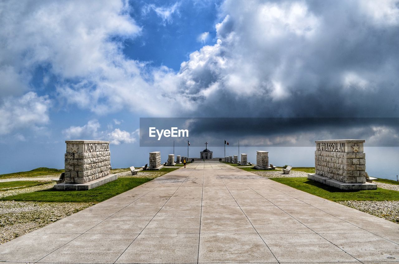 Footpath amidst buildings against cloudy sky