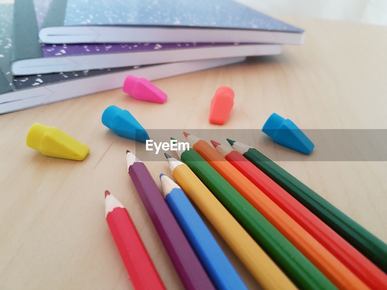 High angle view of colored pencils by erasers and books on table