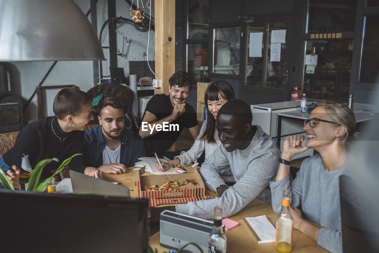 Smiling colleagues eating pizza while working at workplace