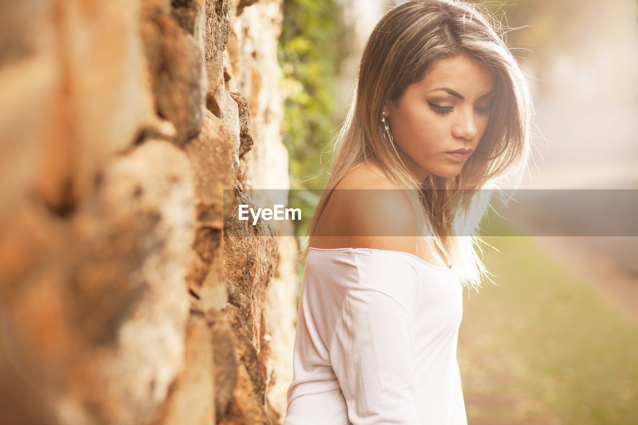 Side view of thoughtful woman standing by wall