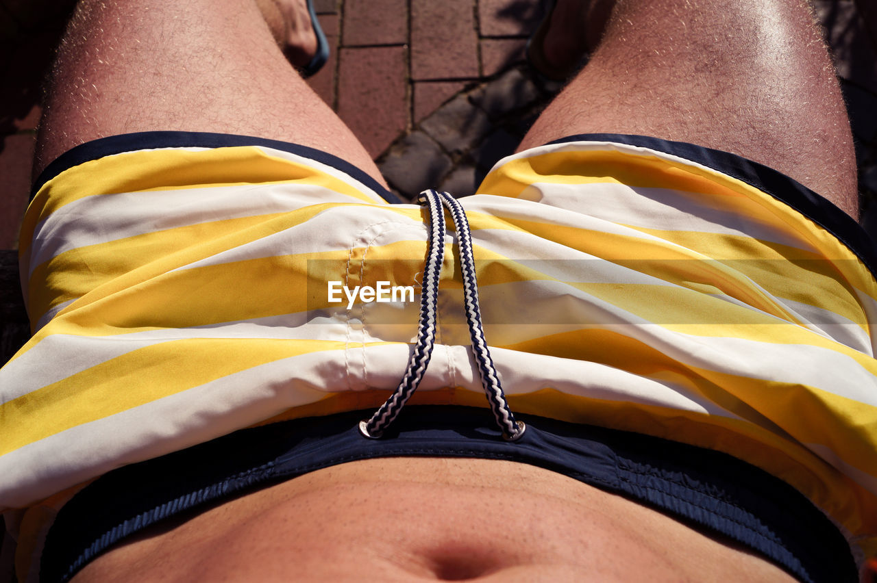 Midsection of shirtless man wearing yellow shorts while resting in yard