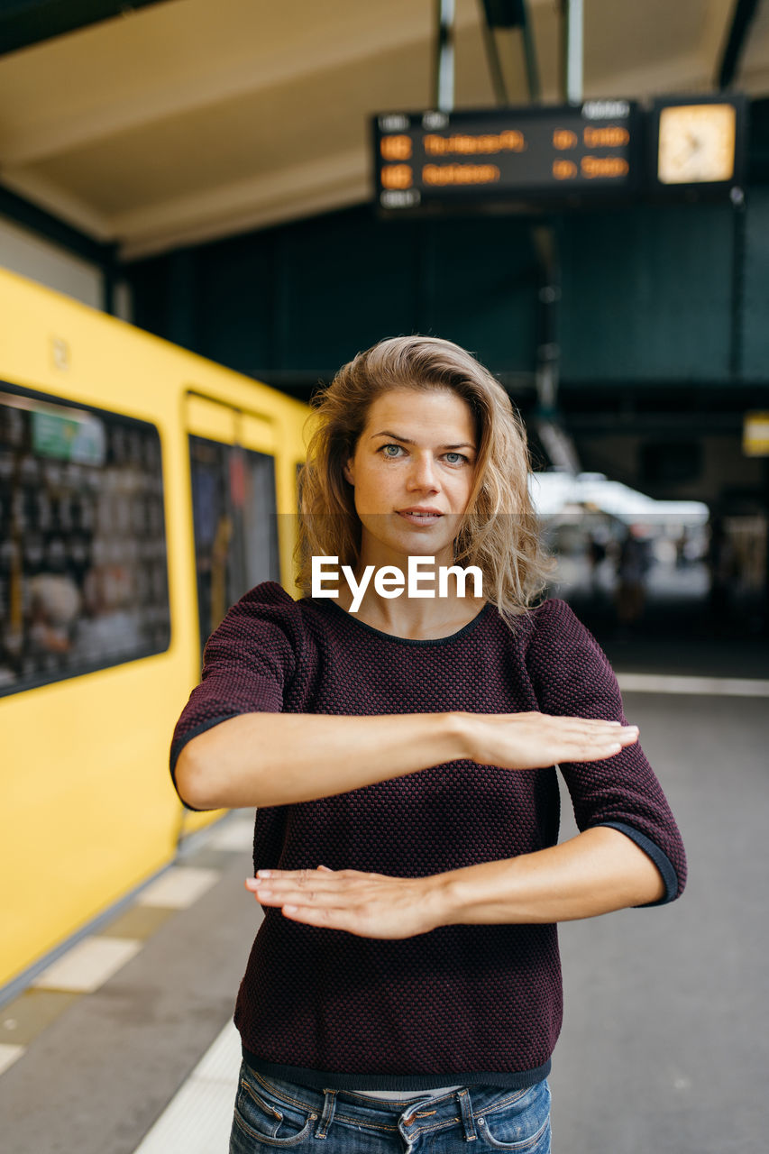 Portrait of woman gesturing equal sign while standing at railroad station platform