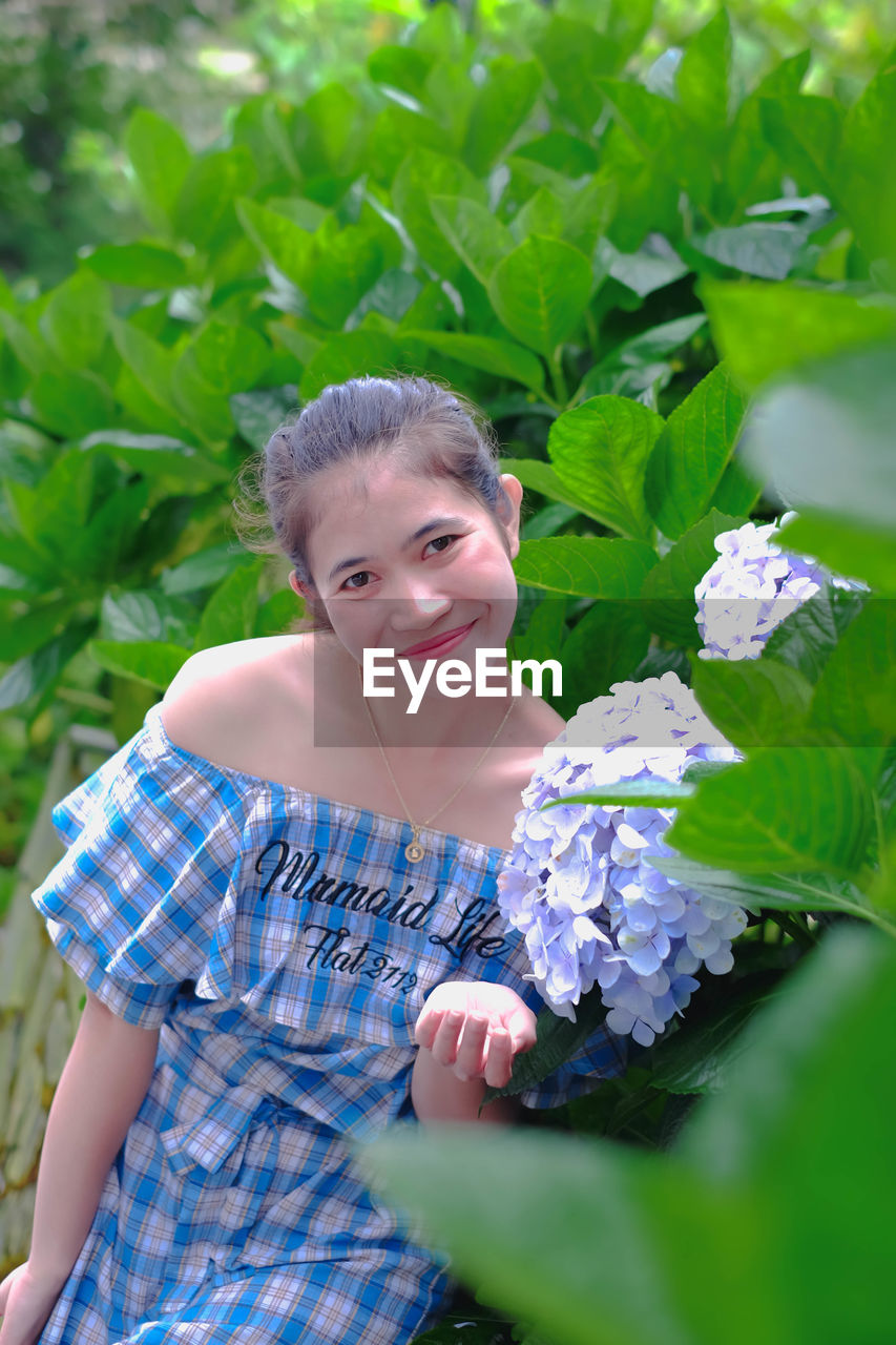 Portrait of young woman standing by flowering plant