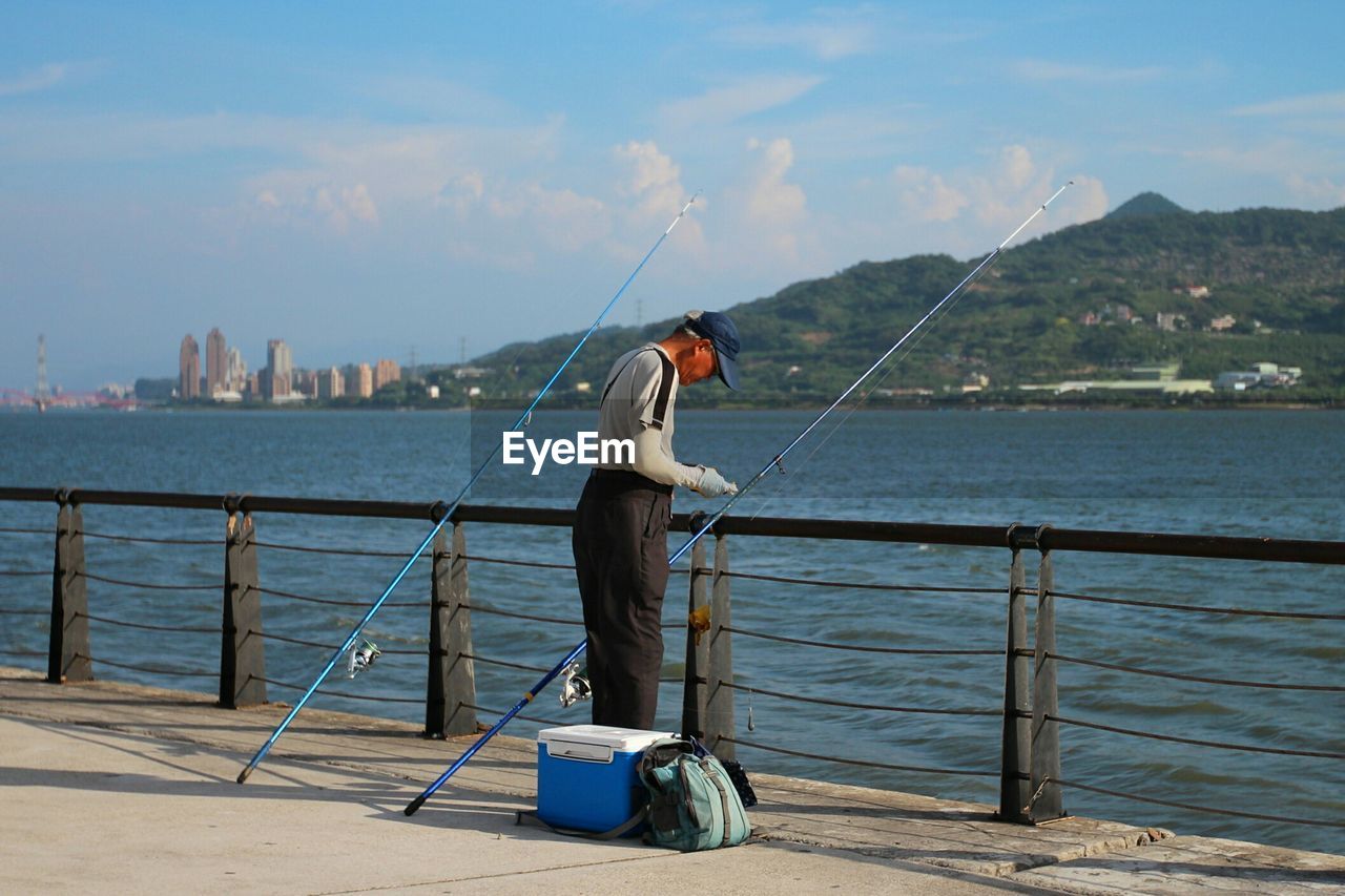 Man fishing by river against sky