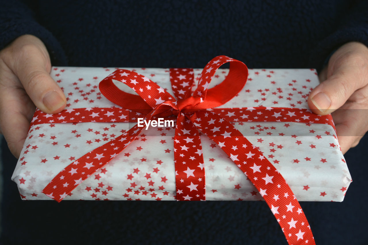 Midsection of woman holding wrapped christmas present with red ribbon