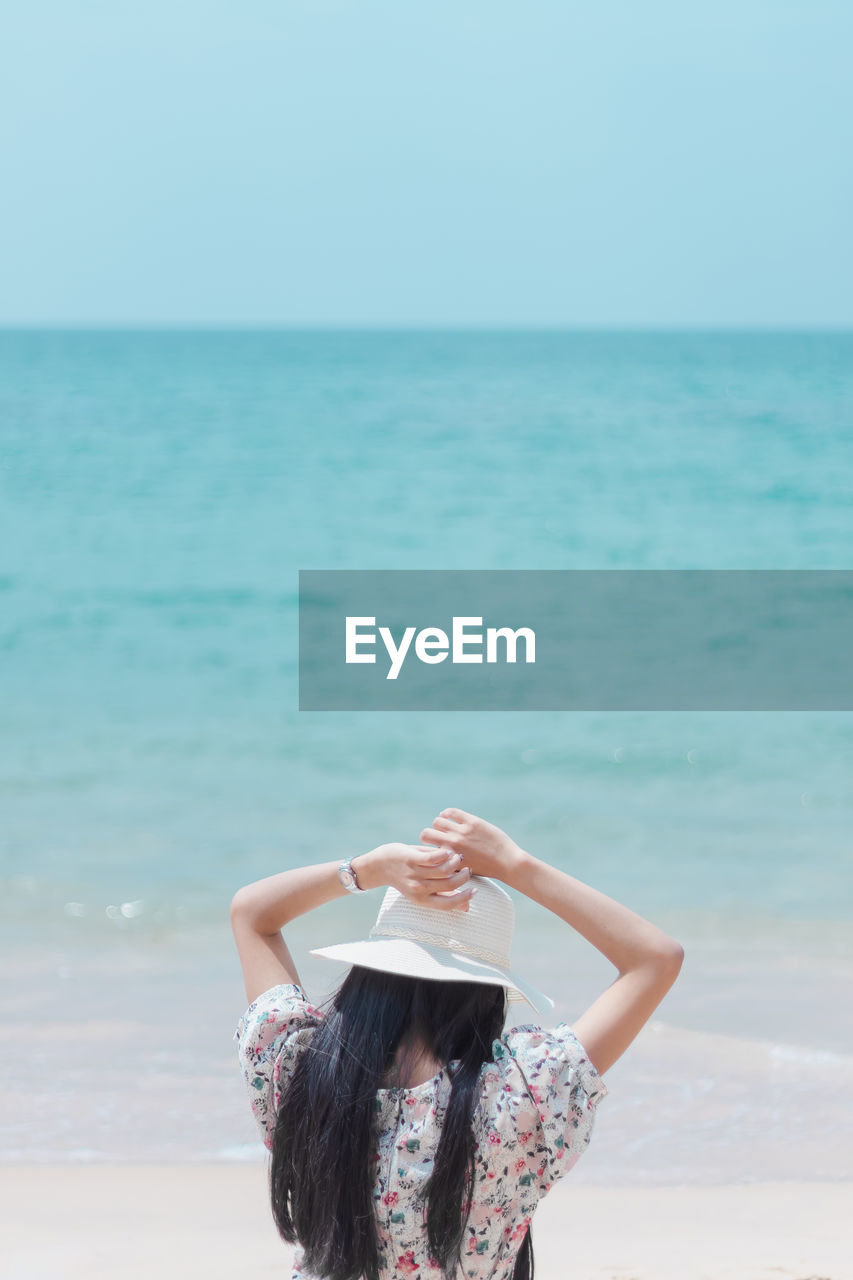 Rear view of woman with arms raised at beach against sky