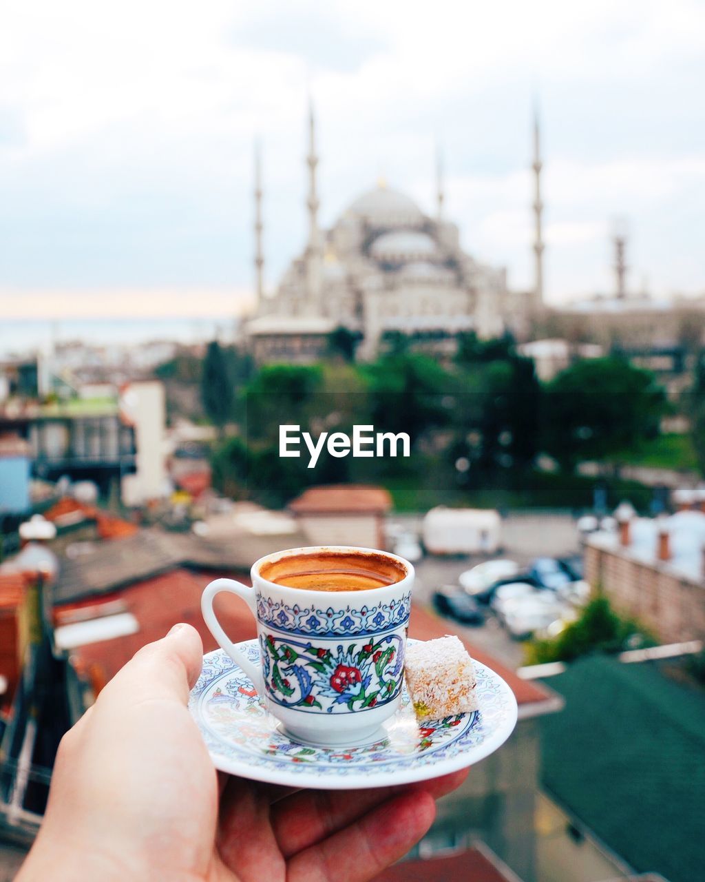 Cropped hand holding tea cup against sultan ahmed mosque in city