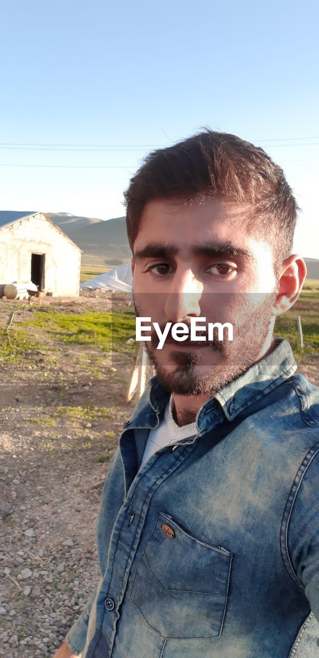 Portrait of young man standing on land against clear sky