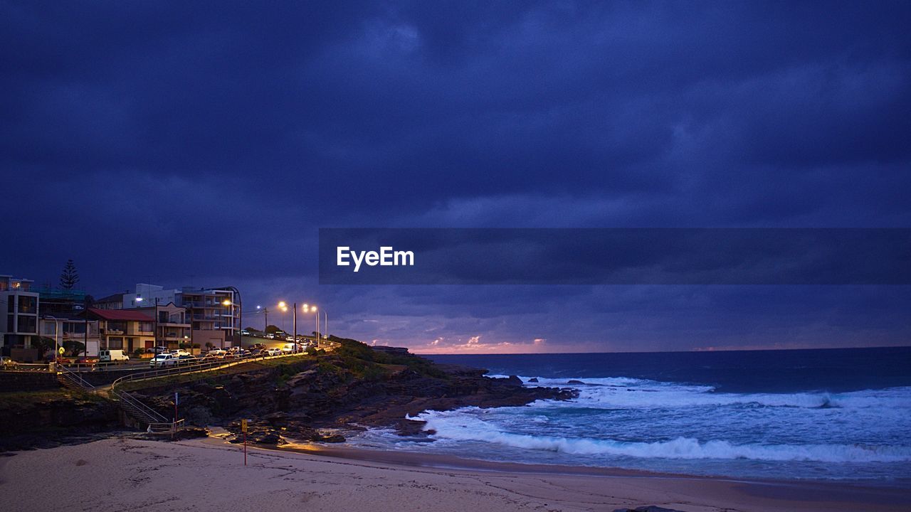 SCENIC VIEW OF ILLUMINATED BEACH AGAINST SKY AT NIGHT