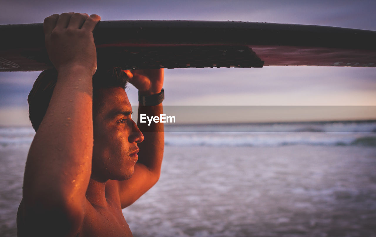 Close-up of man carrying surfboard on head while standing at beach