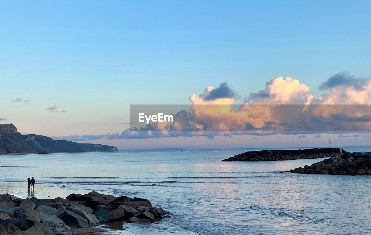 Scenic view of two people looking at sea against sky during sunset