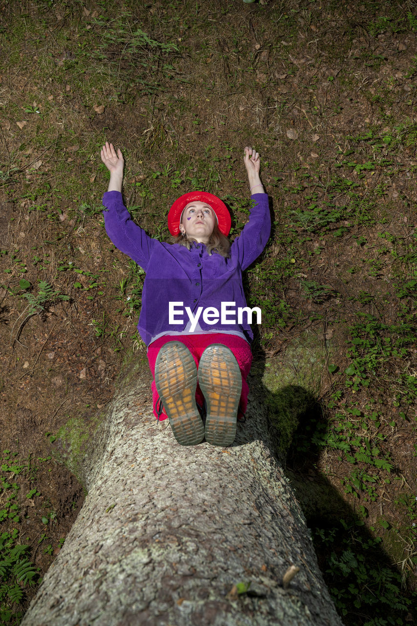 Woman with arms raised sitting on tree trunk