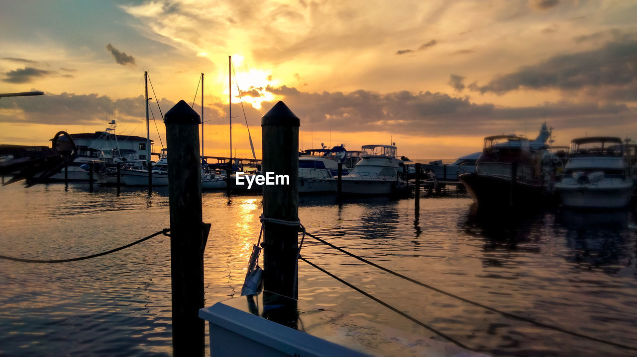 water, sky, sunset, transportation, nautical vessel, cloud, sea, mode of transportation, evening, reflection, nature, dock, dusk, ship, architecture, pier, beauty in nature, harbor, travel destinations, ocean, travel, tranquility, scenics - nature, boat, no people, sun, outdoors, vehicle, moored, tranquil scene, dramatic sky, silhouette, idyllic, built structure, holiday, vacation, sailboat, beach, sunlight, coast, tourism, trip, fishing, orange color, watercraft, building exterior, marina, land, pole, city