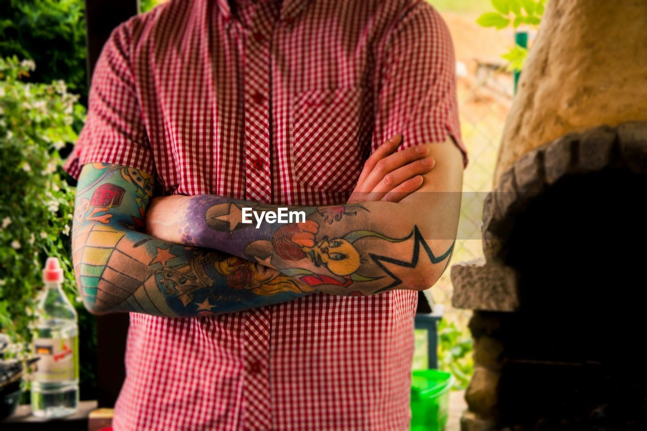 Midsection of man wearing red checked pattern button down shirt with tattoo