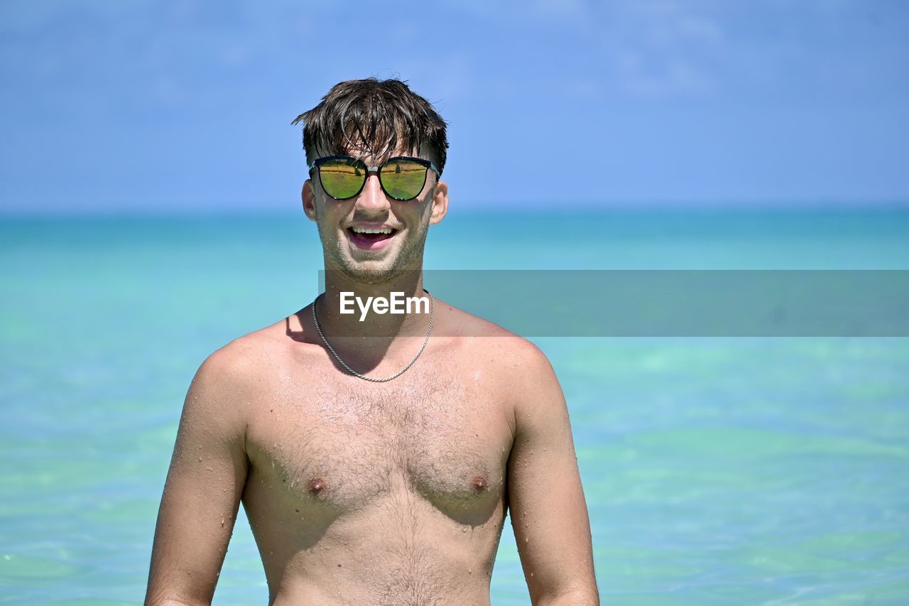 Portrait of shirtless man wearing sunglasses standing at beach