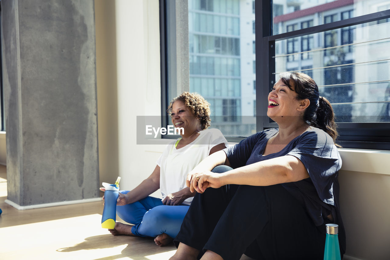 Happy female friends sitting against window in yoga studio