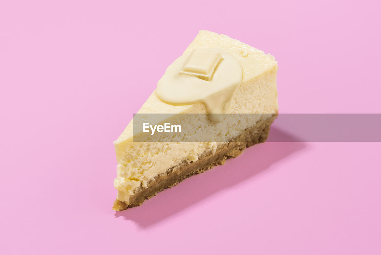 Cheesecake slice with melted white chocolate sauce and creamy filling, isolated on pink  background. 