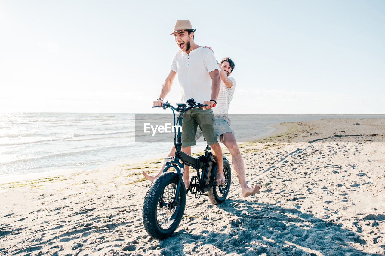 rear view of woman riding bicycles on beach against sky