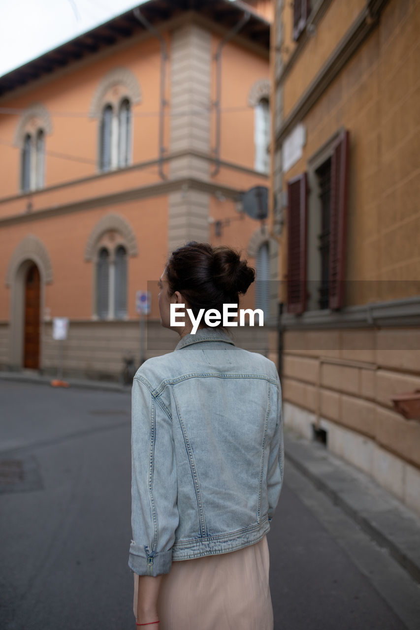 Rear view of woman walking on footpath amidst buildings