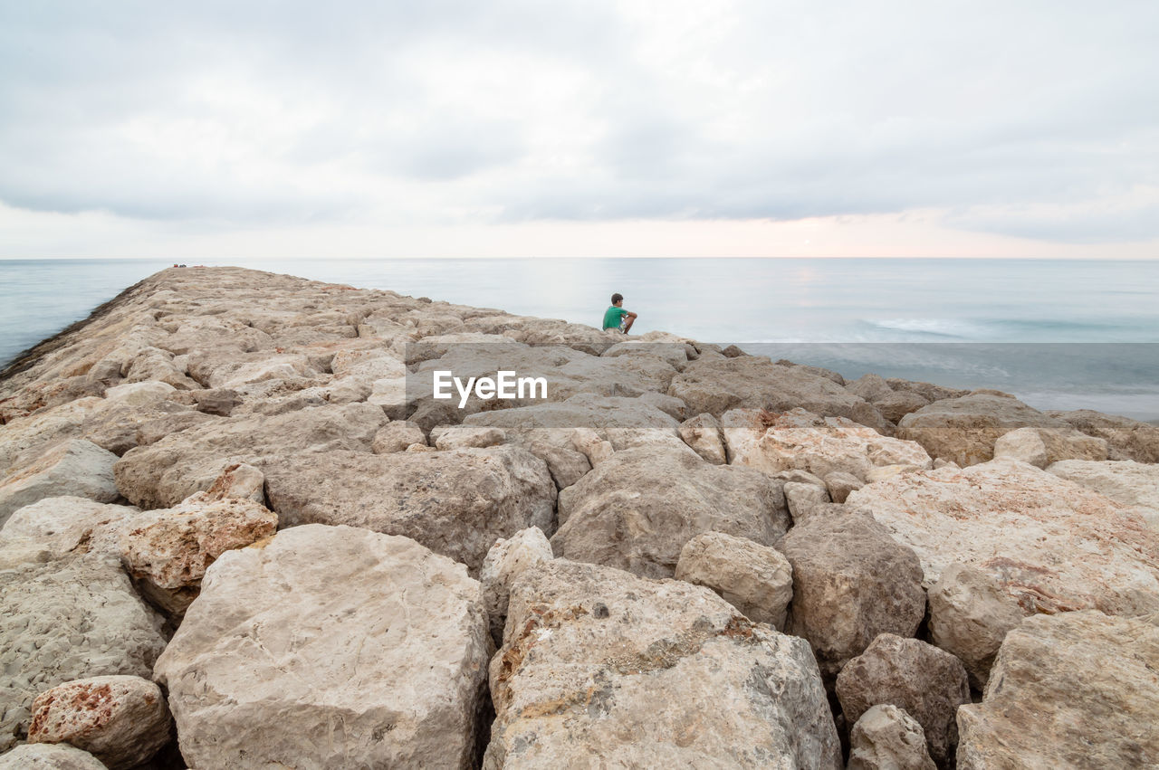 Man sitting on jetty over sea against sky