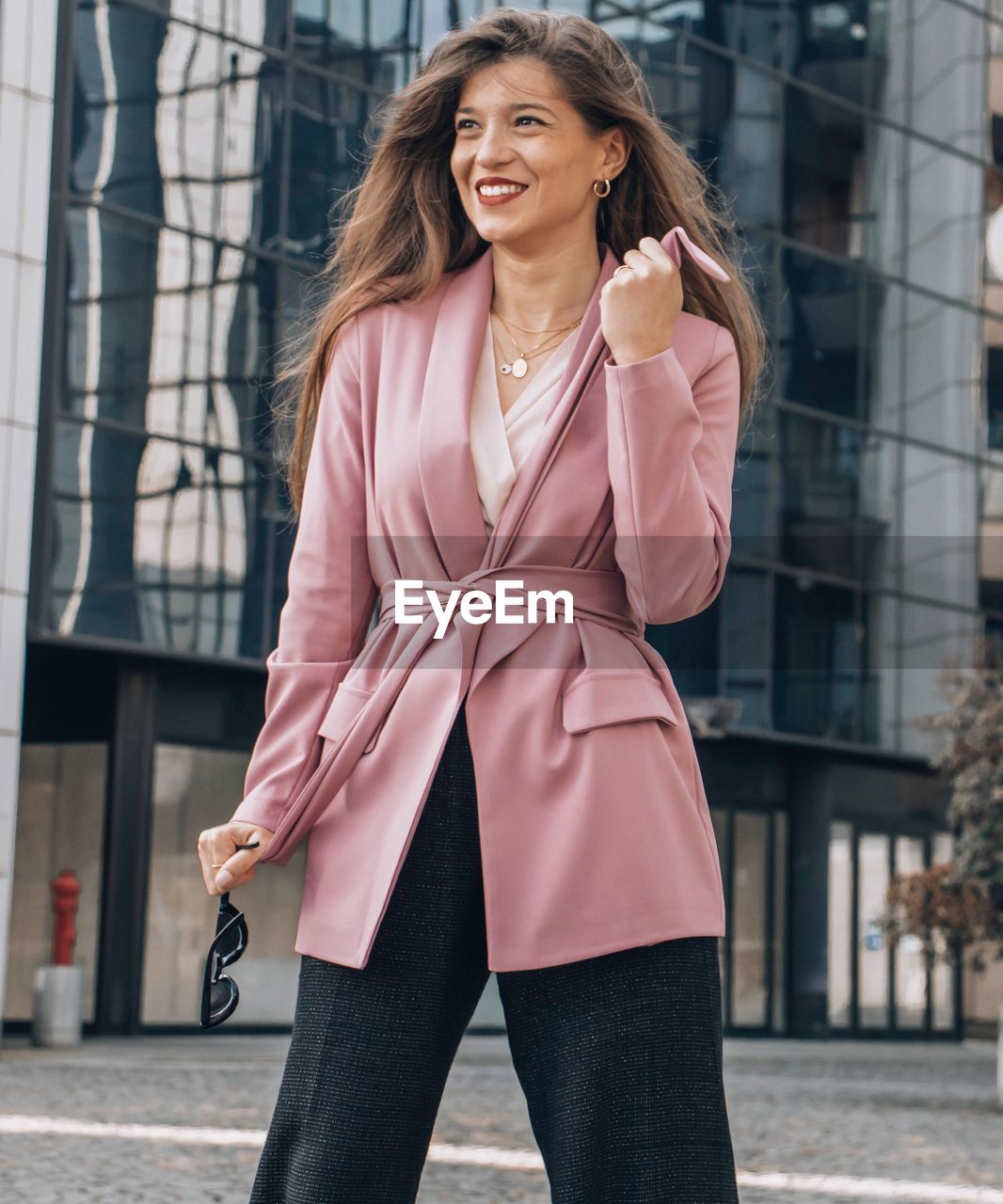 Beautiful young business woman standing against wall in city