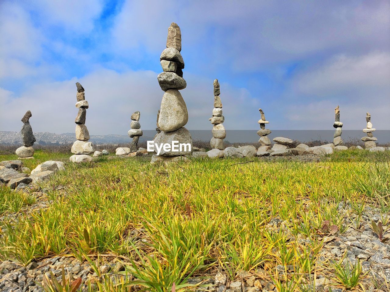 Rock balance on a green grass field with a blue and grey clouds 