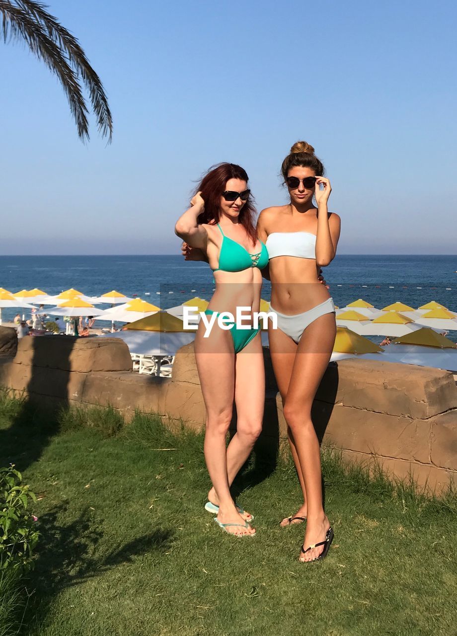 Two women in bikini standing at beach against sky