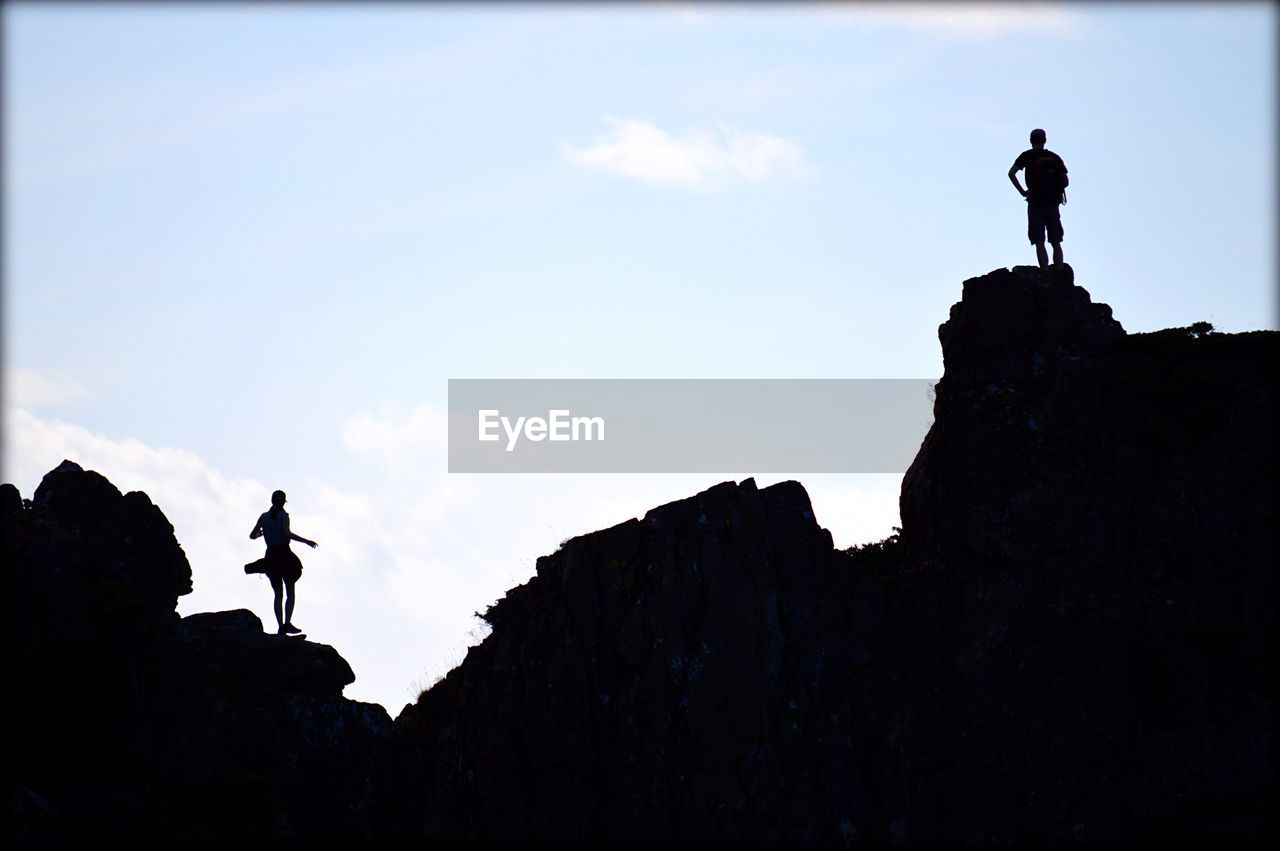 Low angle view of silhouette man and woman standing on rocky mountain against sky