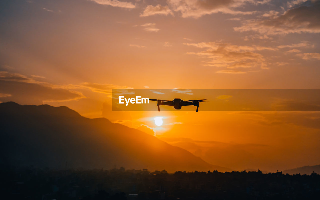 sky, sunset, air vehicle, flying, dawn, transportation, silhouette, airplane, mode of transportation, nature, horizon, sun, cloud, orange color, environment, travel, evening, mountain, sunlight, aircraft, beauty in nature, mid-air, afterglow, scenics - nature, no people, outdoors, drone, motion, technology, landscape, dramatic sky, on the move, vehicle, helicopter, land