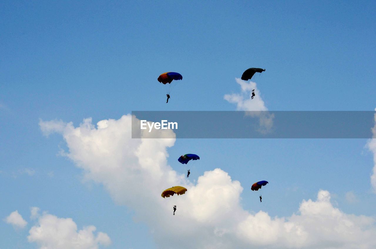 Low angle view of people paragliding against blue sky