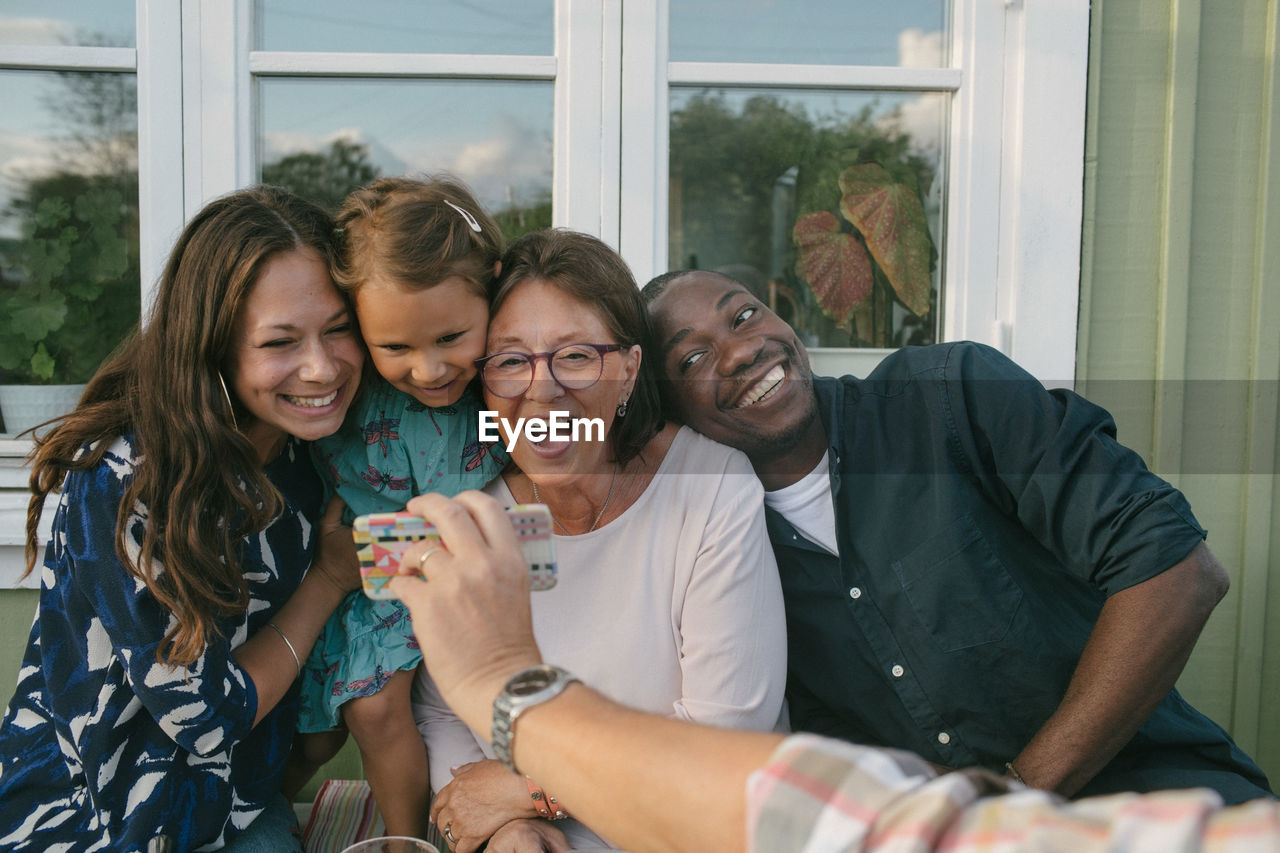 Cropped image of man showing mobile phone to cheerful family on porch
