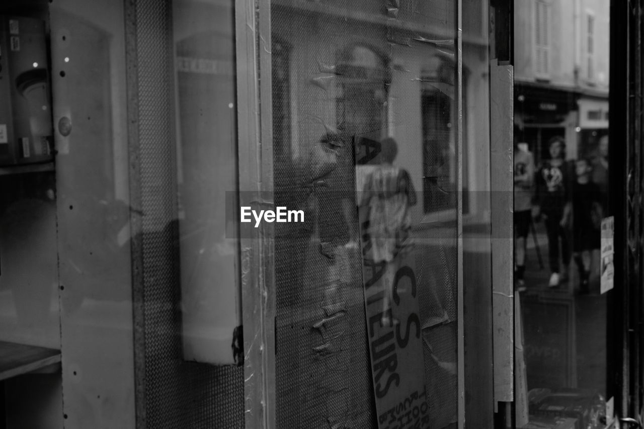 REFLECTION OF MAN PHOTOGRAPHING ON GLASS WINDOW OF STORE