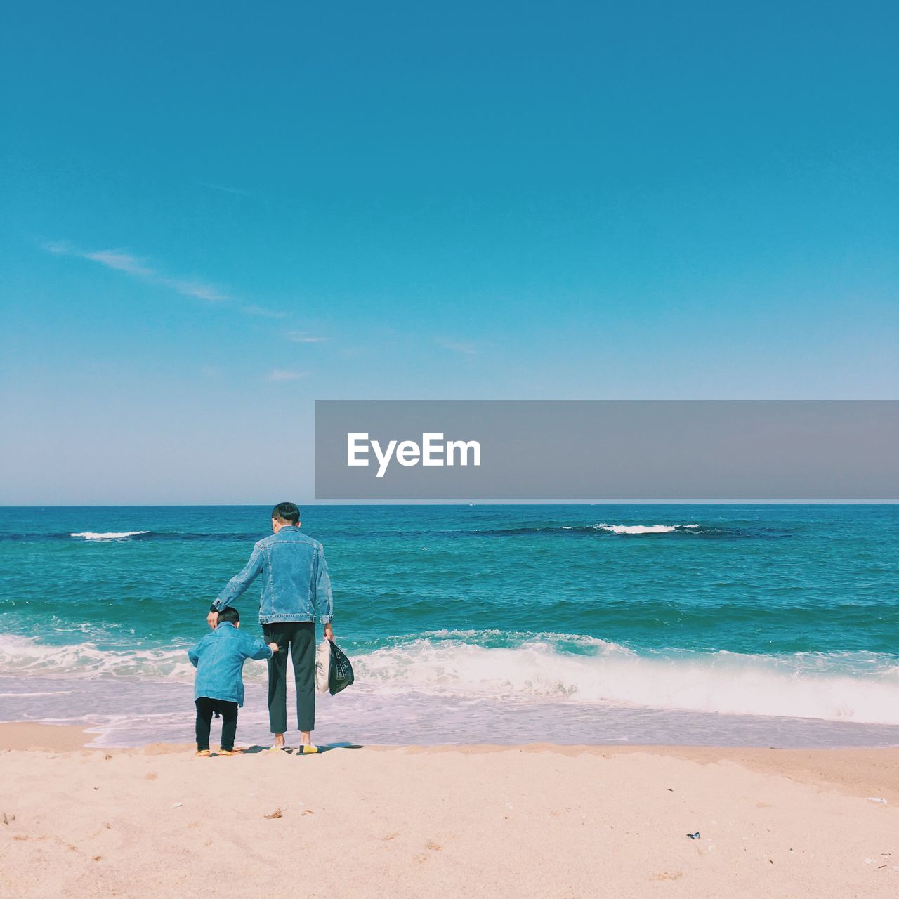 REAR VIEW OF MEN ON BEACH AGAINST BLUE SKY