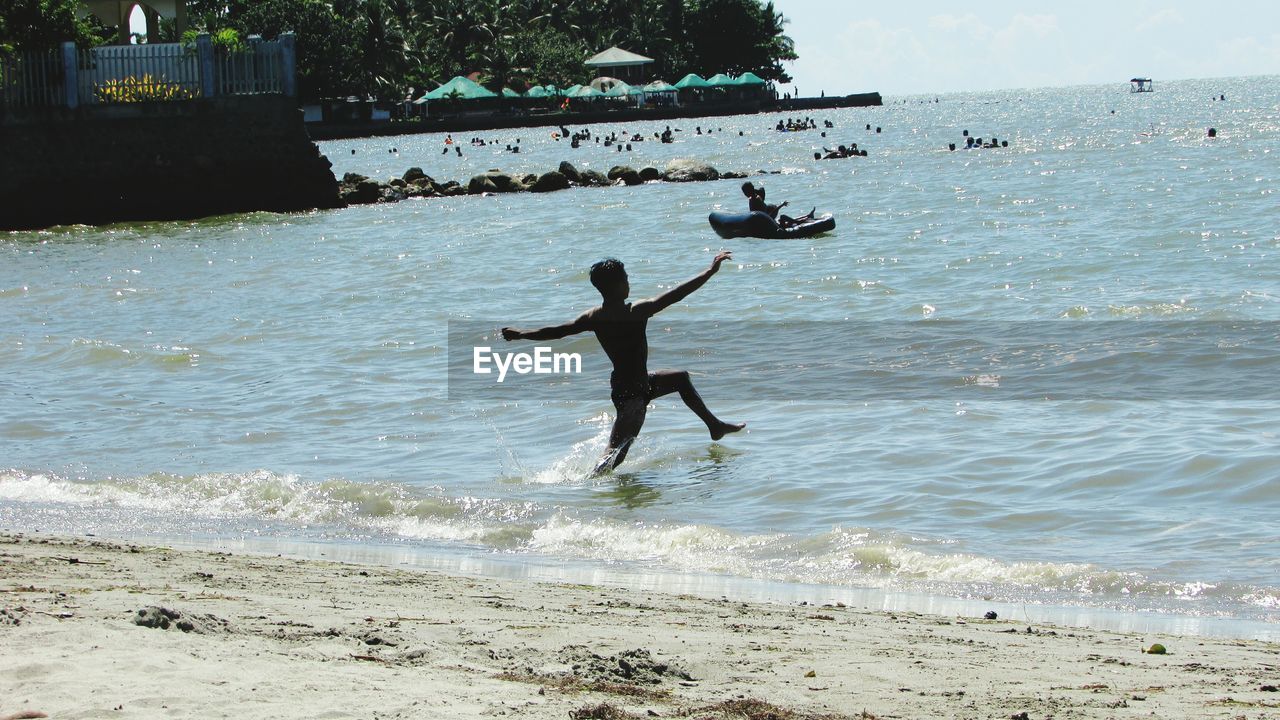 Silhouette shirtless man running in sea during sunny day
