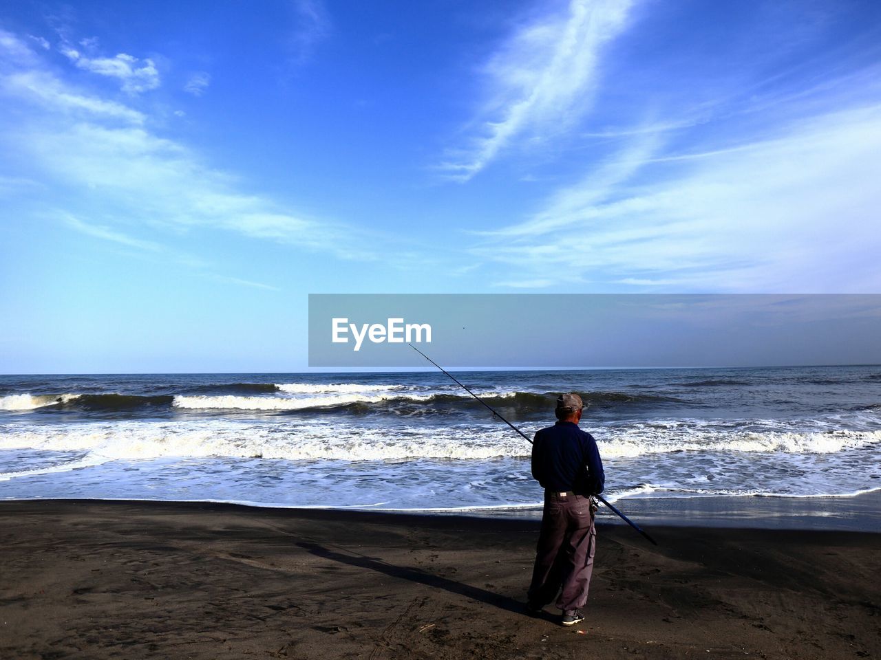 Person standing on beach with fishing pole