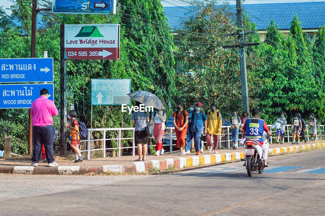 transportation, sign, road, city, group of people, men, tree, street, endurance sports, day, plant, architecture, communication, text, nature, vehicle, mode of transportation, women, adult, race, crowd, lifestyles, bicycle, person, land vehicle, cycling, outdoors, road sign, built structure, large group of people, symbol, western script, building exterior, leisure activity