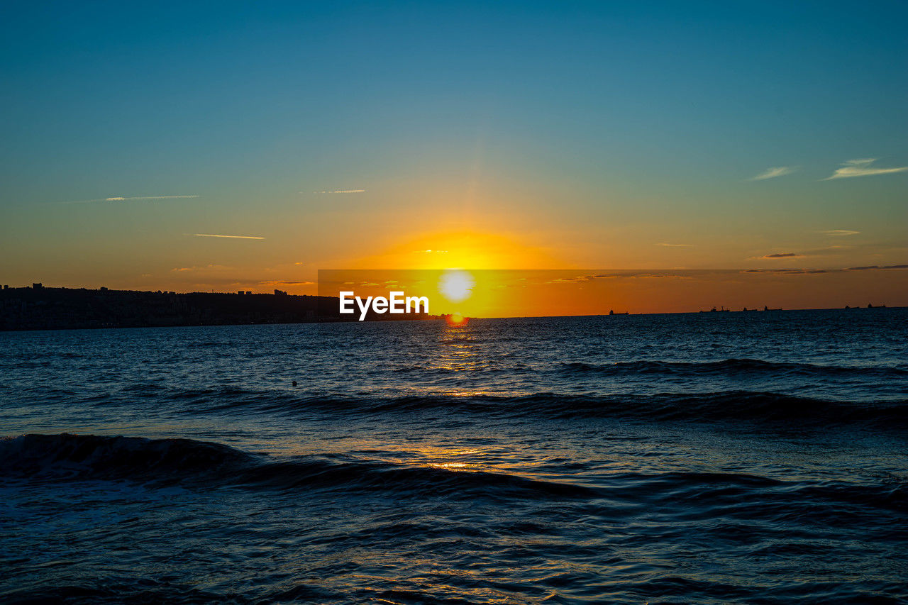 sky, sea, water, sunset, beauty in nature, scenics - nature, ocean, tranquility, nature, horizon over water, horizon, sun, tranquil scene, idyllic, sunlight, afterglow, orange color, land, wind wave, seascape, wave, cloud, beach, no people, dramatic sky, motion, environment, coast, shore, outdoors, travel, blue, sunbeam, travel destinations, urban skyline, dusk, reflection, evening, non-urban scene, landscape, silhouette, rippled, vacation, atmospheric mood, summer, trip