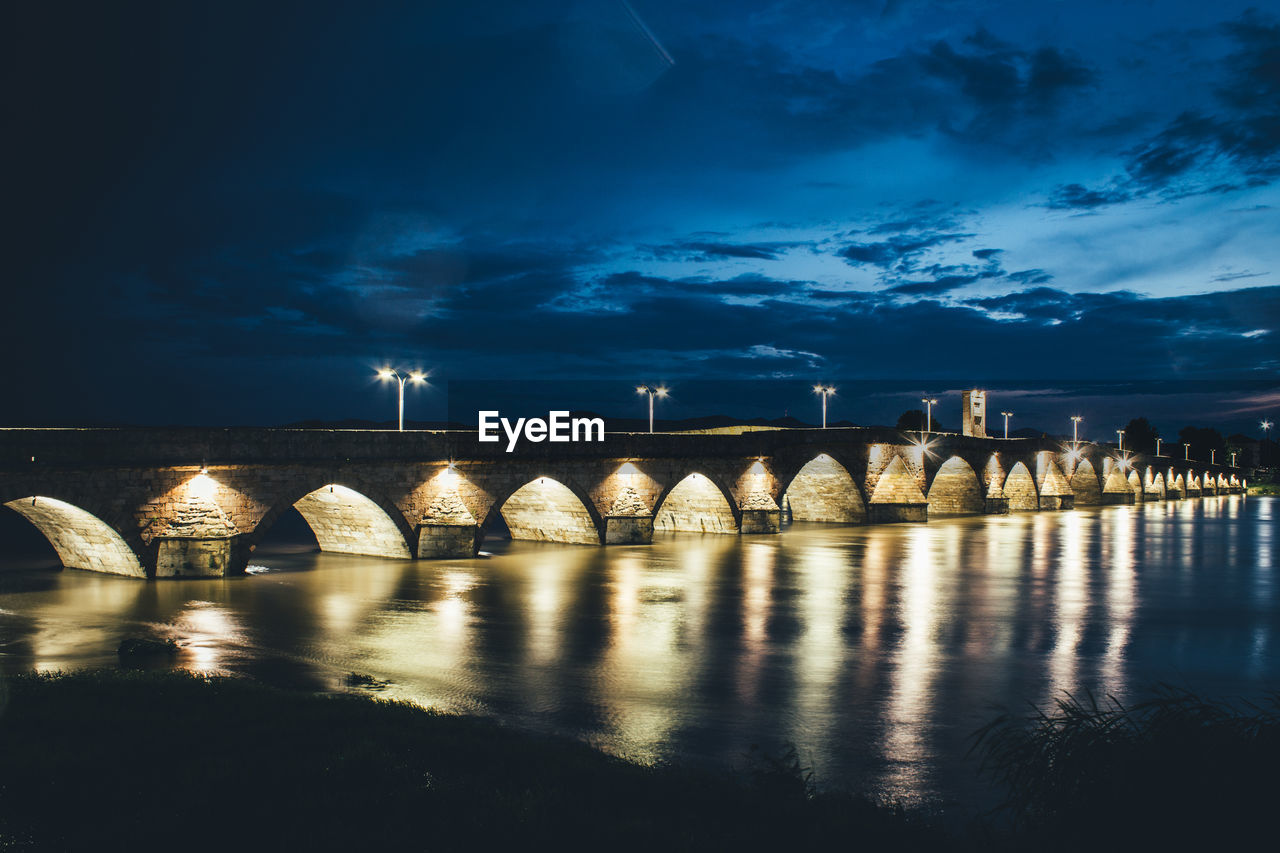 Illuminated bridge over water against blue sky at night