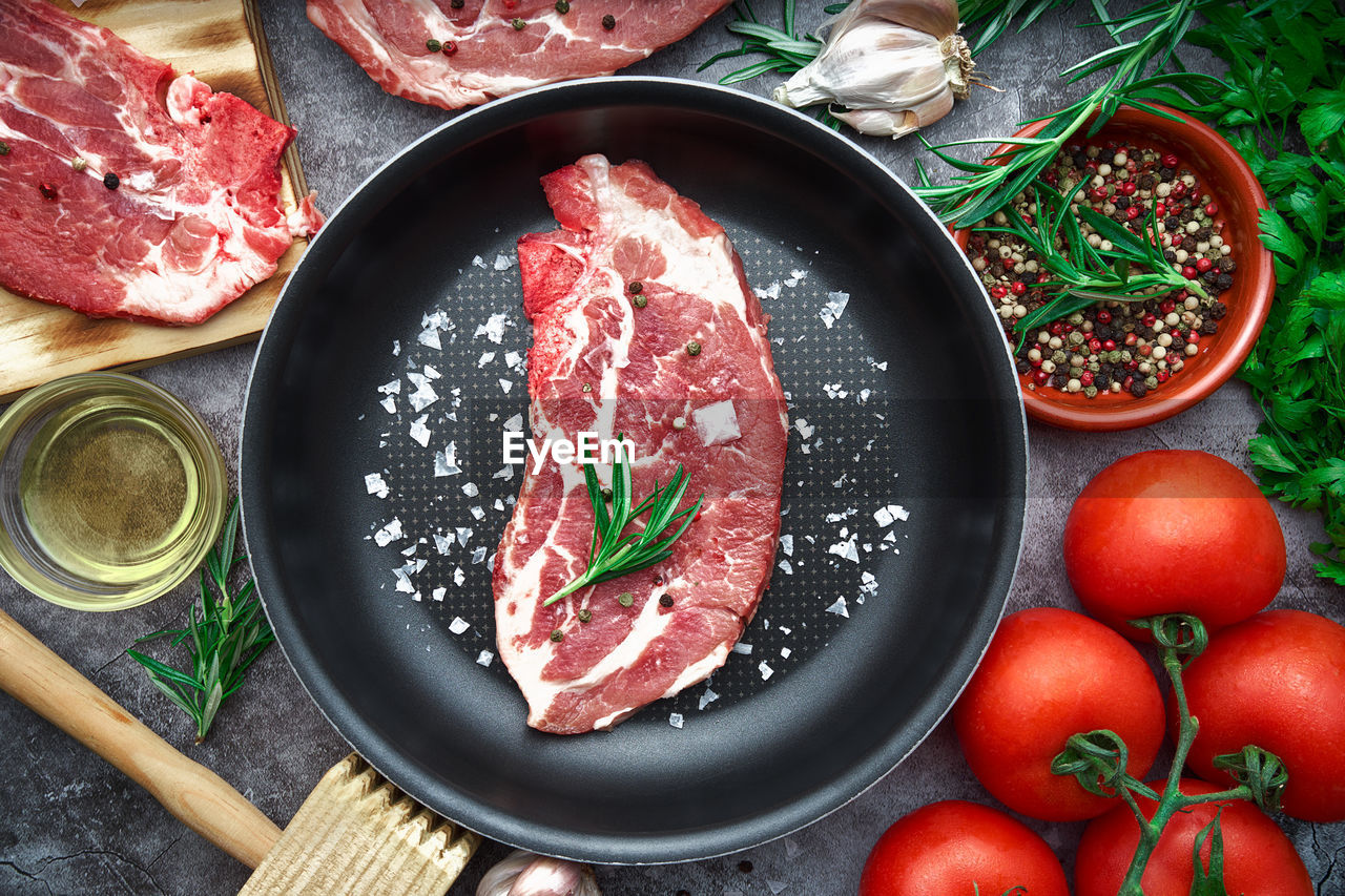 Raw beef steak with tomato, garlic, pepper, salt and rosemary on frying pan on a dark background.